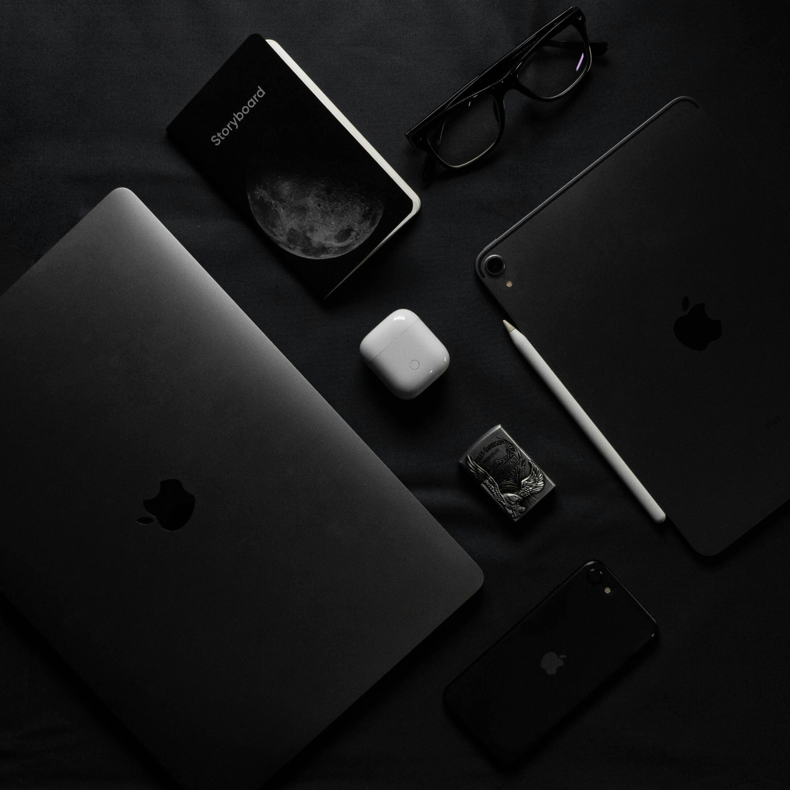 A dark minimalist flatlay of modern gadgets including laptop, smartphone, and eyeglasses.